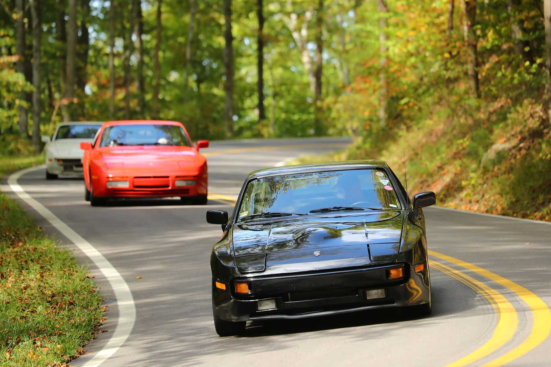 A line of Porsche 944s carving through a forest curve near the Tail of the Dragon