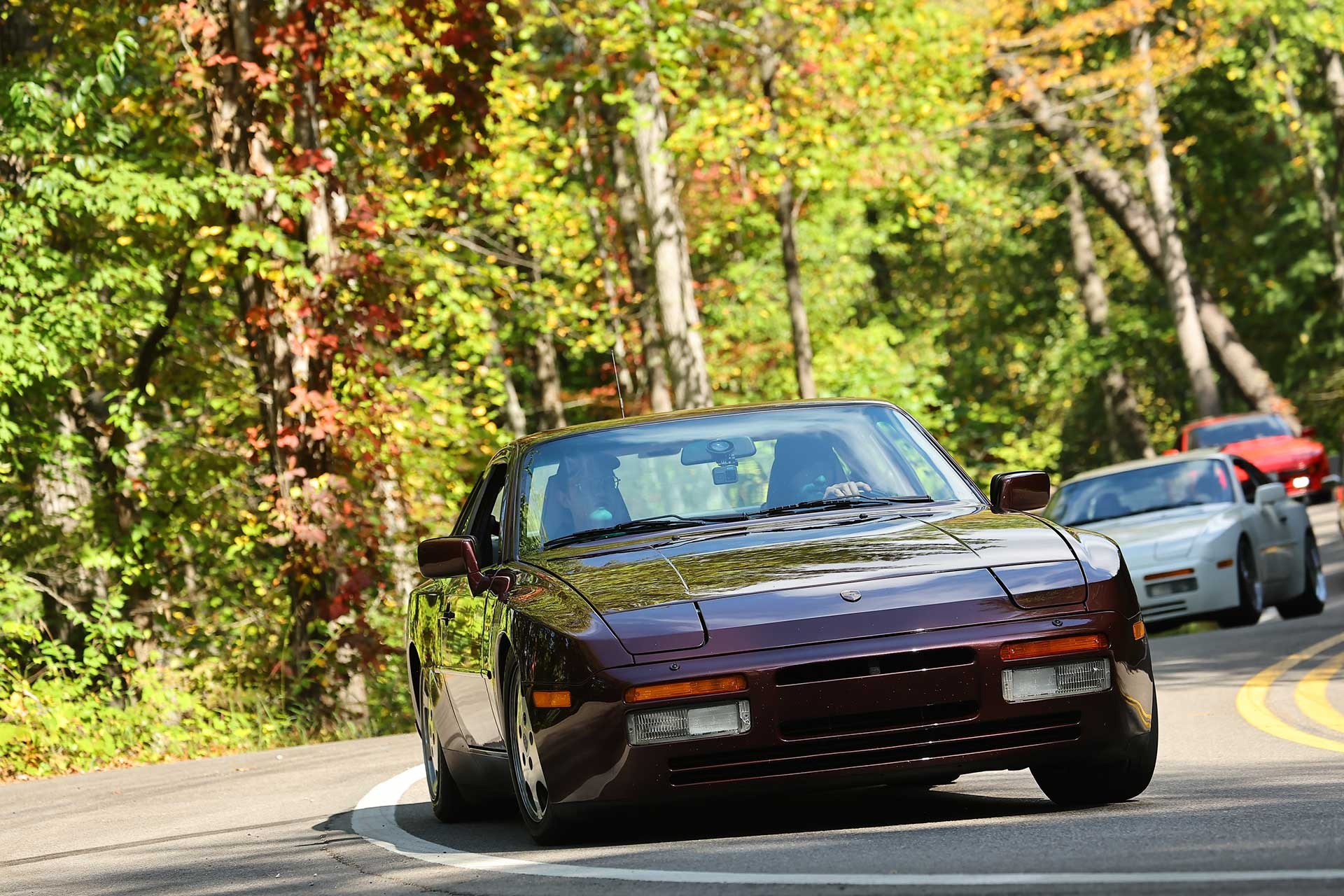 A maroon Porsche 944 Turbo leading a group through fall color on the Dragon