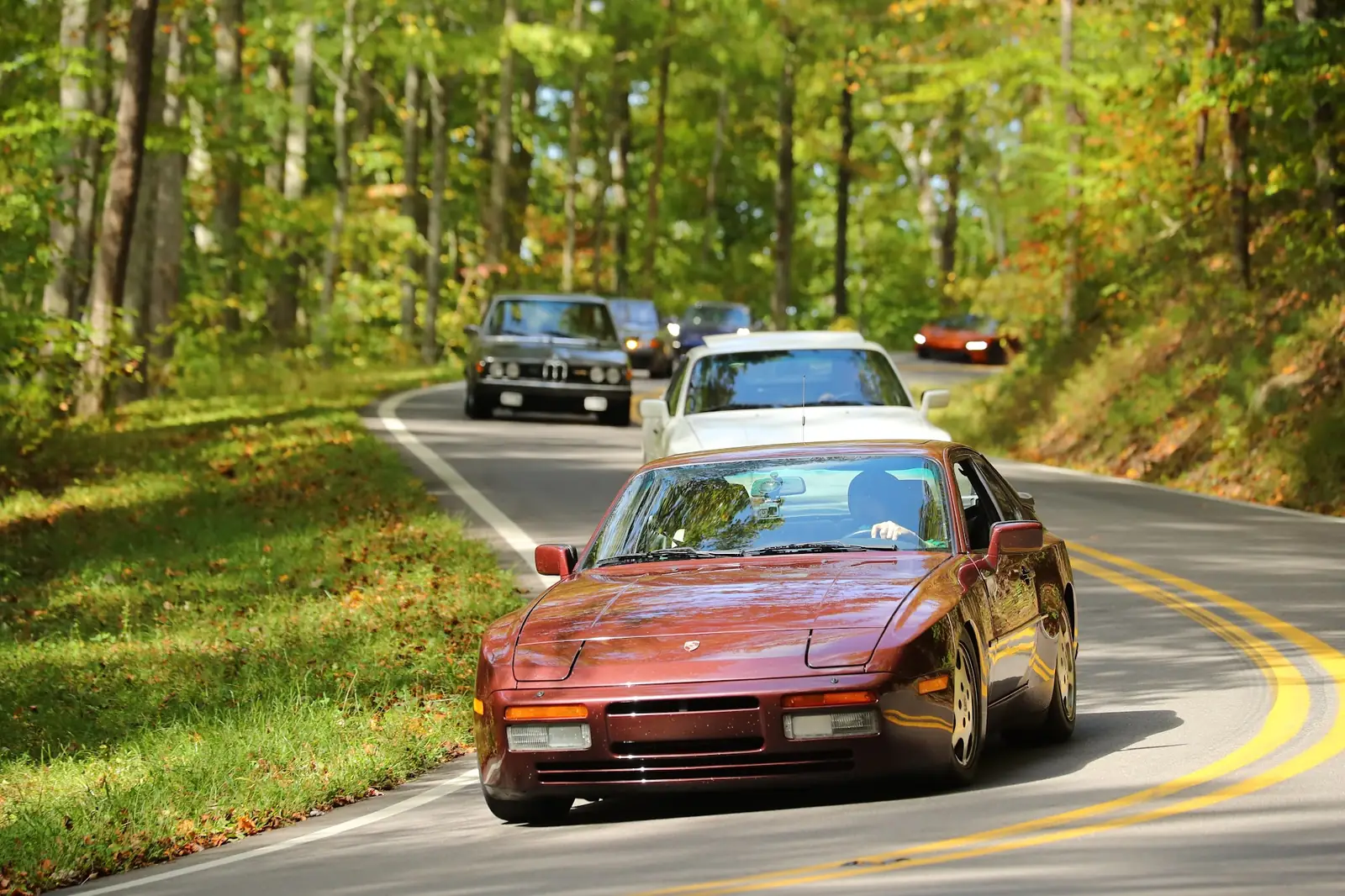 A maroon 944 leading a line of cars through an S-curve on the Dragon