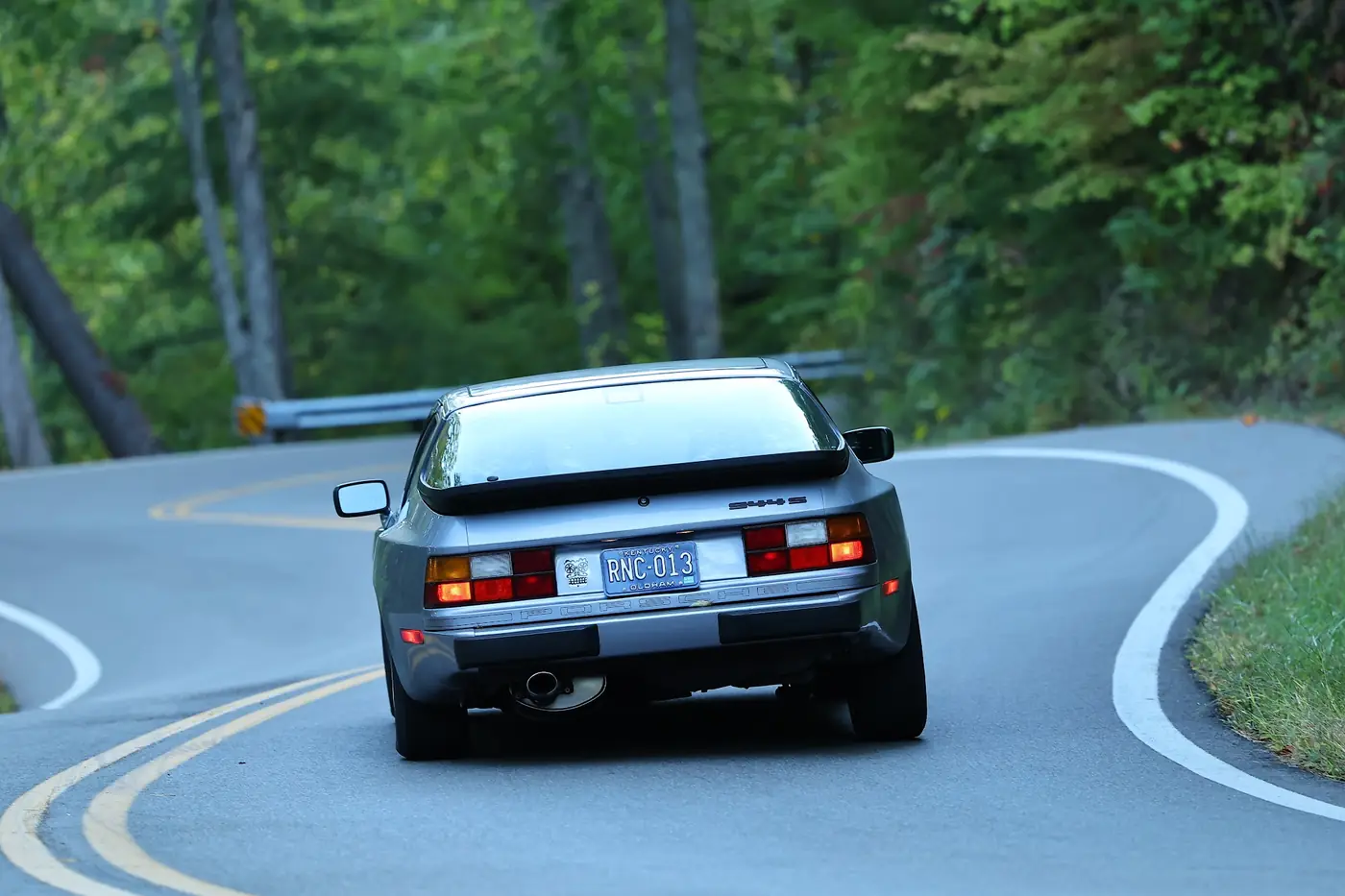 A grey 944 in its lane through an S-curve, double yellow line on one side and the white line on the other